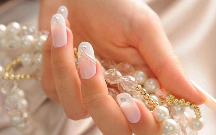 Idea per delle unghie gel bianche brillantini, manicure a mandorla. collana di perle in mano di una donna 