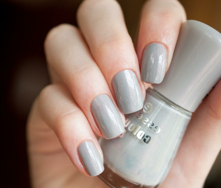 Unghie gel bellissime di colore grigio effetto lucido, bottiglietta di smalto tra le mani